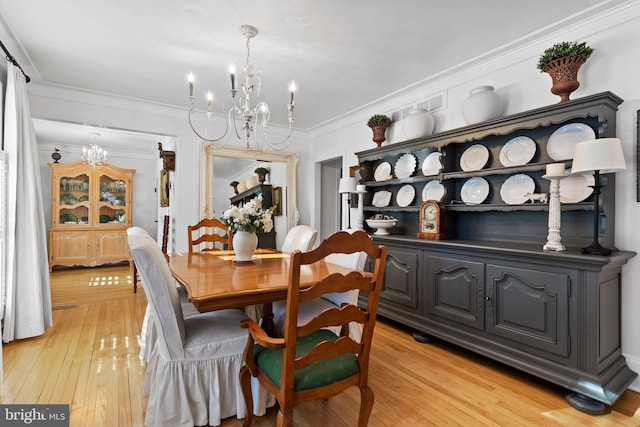 dining room with a notable chandelier, ornamental molding, and light wood-type flooring