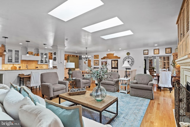 living room with an inviting chandelier, a skylight, light hardwood / wood-style flooring, and ornamental molding