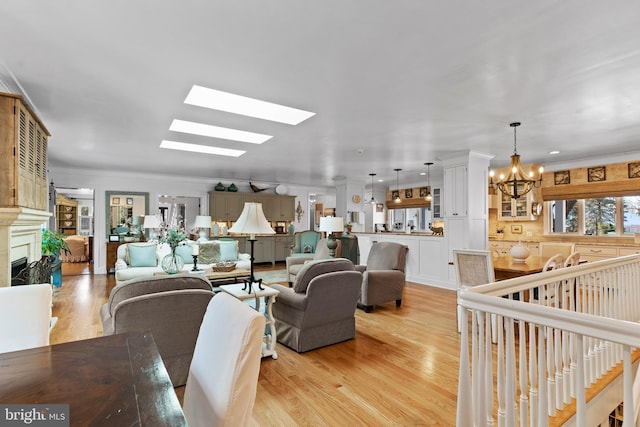 living room with a notable chandelier, ornamental molding, light hardwood / wood-style floors, and a skylight