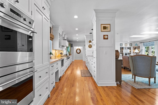 kitchen with white cabinetry, crown molding, light hardwood / wood-style floors, and stainless steel double oven