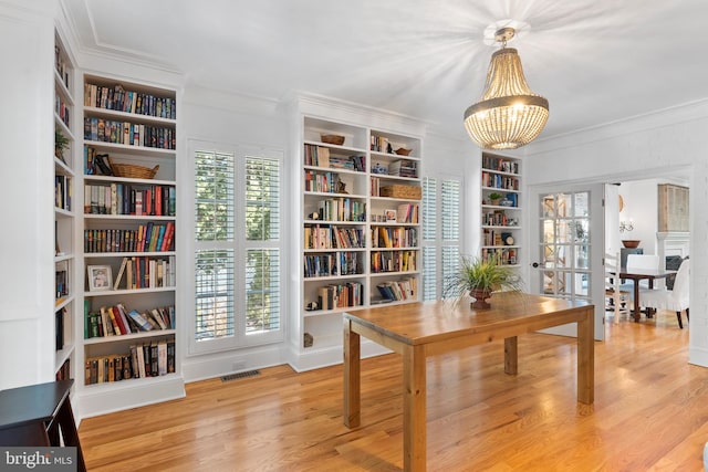 interior space featuring built in features, wood-type flooring, ornamental molding, and a chandelier