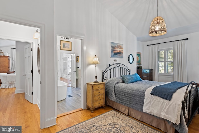 bedroom featuring ensuite bath, wood-type flooring, and high vaulted ceiling