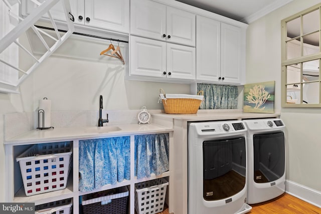 washroom featuring sink, washing machine and dryer, crown molding, cabinets, and light hardwood / wood-style floors