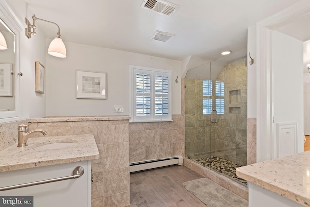 bathroom featuring walk in shower, tile walls, a baseboard radiator, vanity, and hardwood / wood-style floors