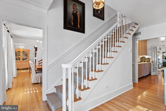 stairs featuring hardwood / wood-style flooring, ornamental molding, and a chandelier