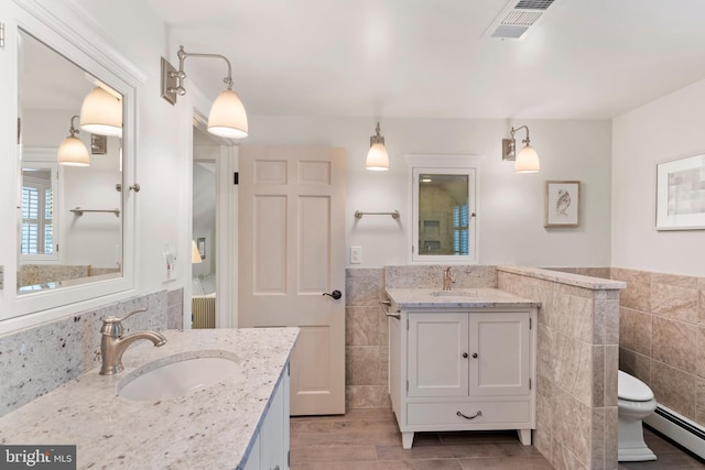 bathroom featuring baseboard heating, tile walls, radiator heating unit, vanity, and toilet