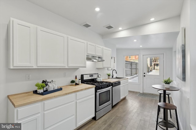 kitchen with sink, wooden counters, light wood-type flooring, stainless steel appliances, and white cabinets