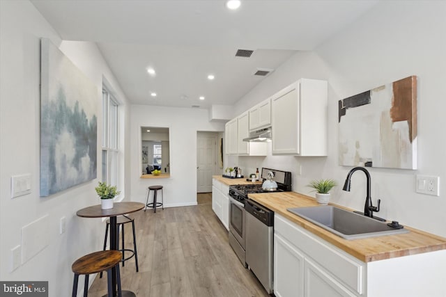 kitchen featuring appliances with stainless steel finishes, butcher block counters, sink, white cabinets, and light wood-type flooring