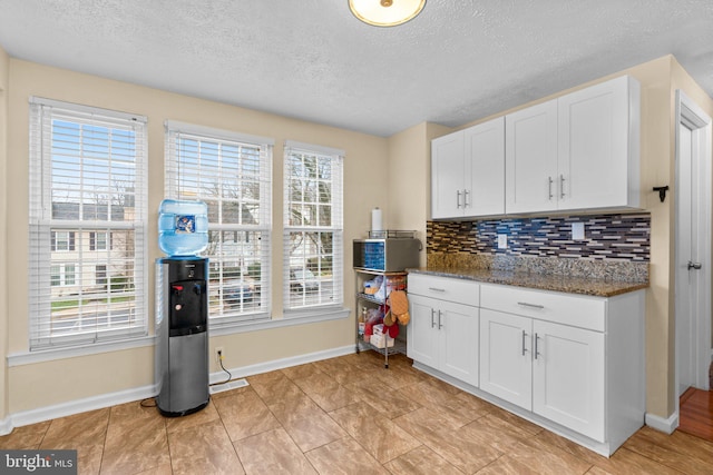 kitchen with white cabinetry, backsplash, a textured ceiling, and dark stone countertops