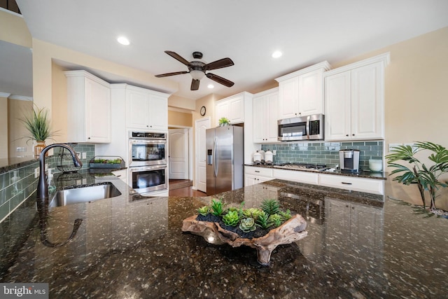 kitchen featuring sink, white cabinetry, dark stone countertops, stainless steel appliances, and backsplash