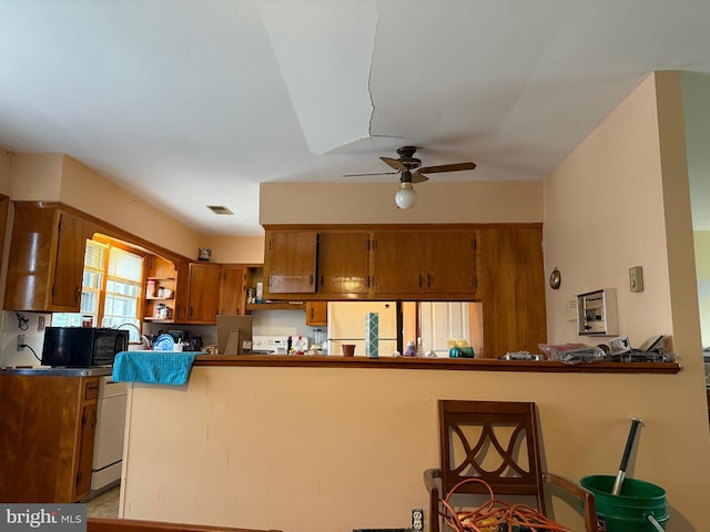 kitchen with a peninsula, black microwave, brown cabinets, ceiling fan, and fridge