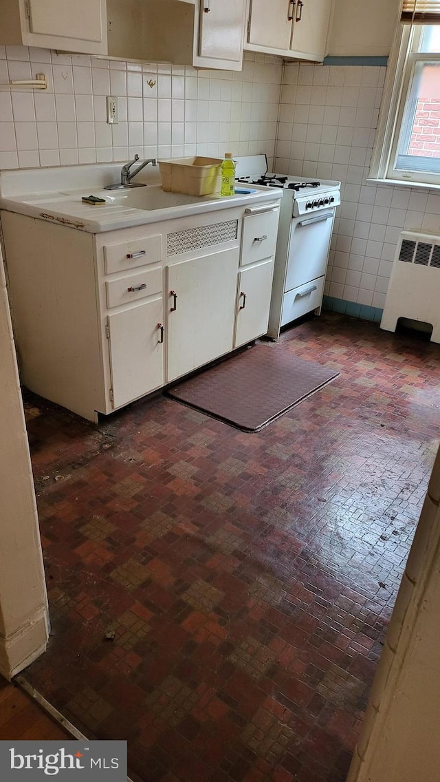 kitchen featuring sink, gas range gas stove, white cabinetry, radiator, and backsplash