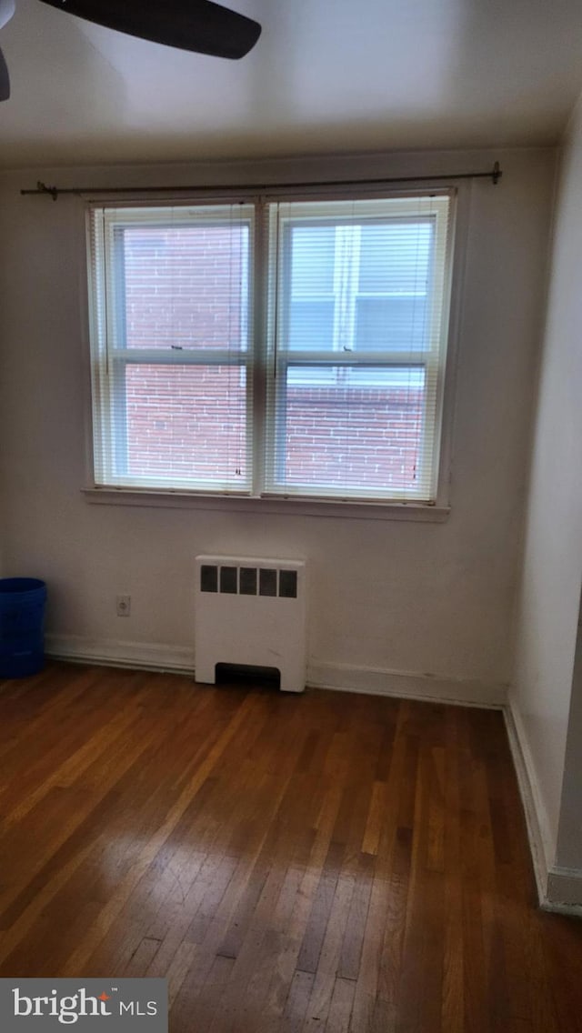 unfurnished room with dark hardwood / wood-style floors, radiator, and a wealth of natural light