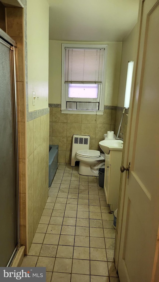 bathroom featuring toilet, heating unit, tile walls, vanity, and tile patterned flooring