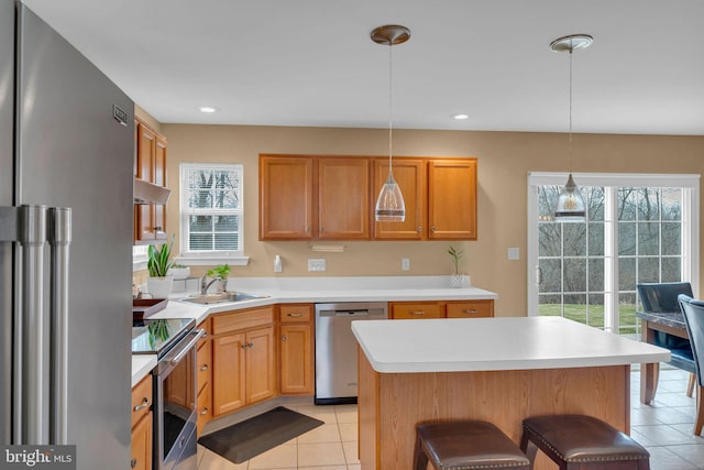 kitchen featuring a kitchen bar, sink, hanging light fixtures, a kitchen island, and stainless steel appliances