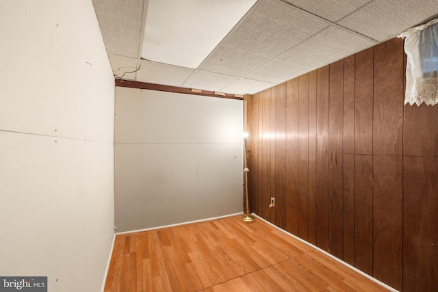 basement featuring hardwood / wood-style flooring, a paneled ceiling, and wooden walls