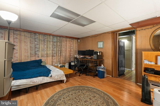 bedroom featuring wood-type flooring, a drop ceiling, and wood walls