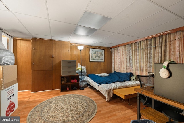 bedroom featuring a paneled ceiling, wooden walls, and hardwood / wood-style floors