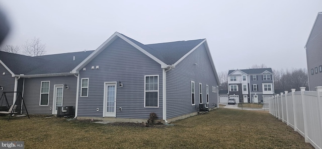 rear view of house with central AC unit, a lawn, and fence