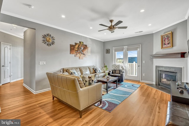 living room with ceiling fan, ornamental molding, a premium fireplace, and light hardwood / wood-style floors