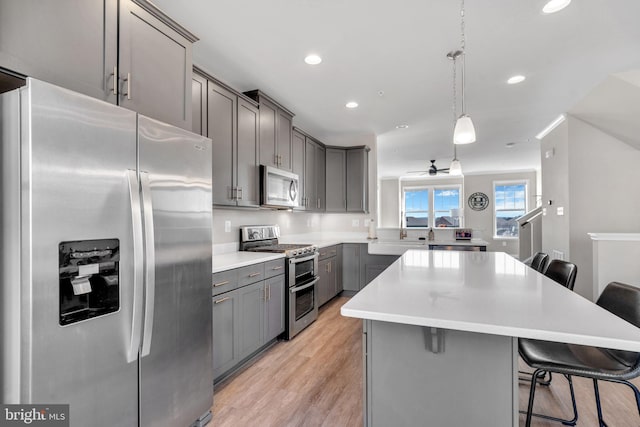 kitchen featuring a breakfast bar, gray cabinetry, a center island, appliances with stainless steel finishes, and pendant lighting