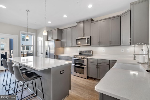 kitchen with gray cabinets, hanging light fixtures, stainless steel appliances, a center island, and light wood-type flooring