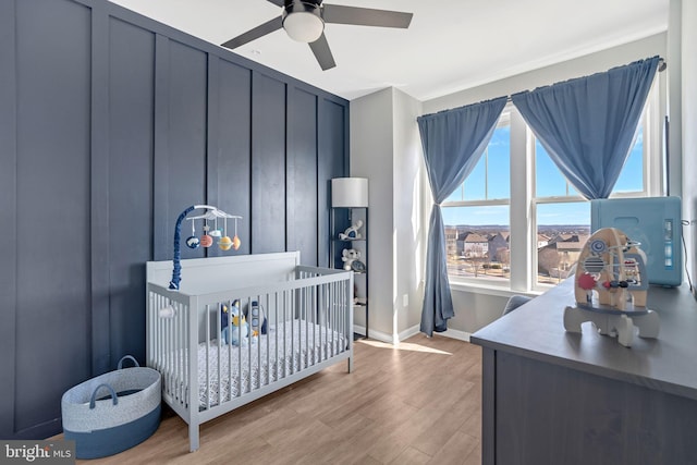 bedroom with a crib, ceiling fan, and light hardwood / wood-style flooring