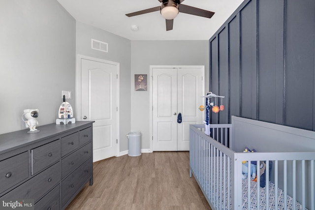 bedroom featuring a nursery area, a closet, ceiling fan, and light hardwood / wood-style flooring