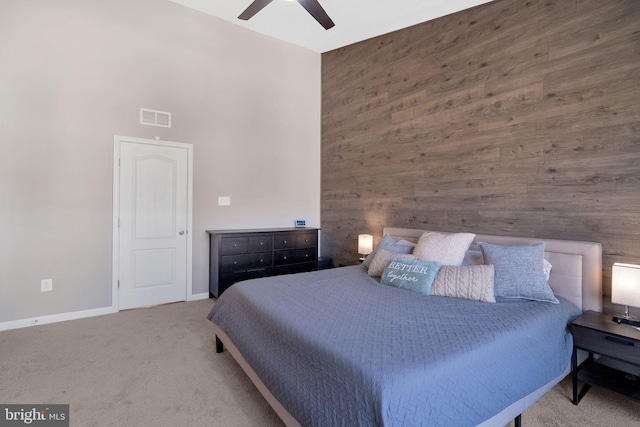 carpeted bedroom with ceiling fan, wooden walls, and a high ceiling