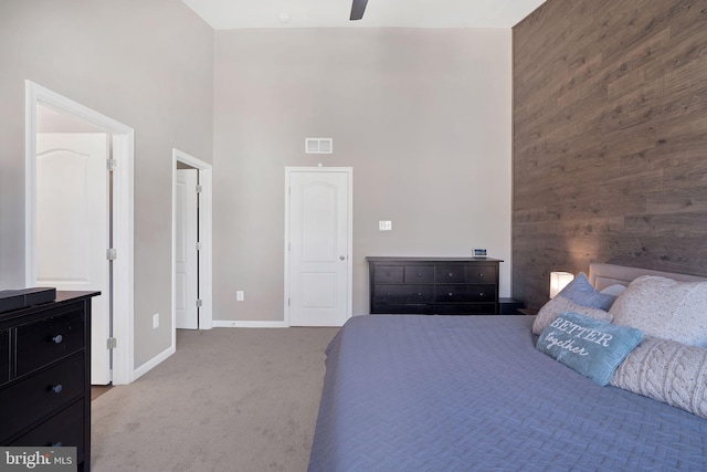 bedroom featuring ceiling fan, carpet flooring, wooden walls, and a towering ceiling