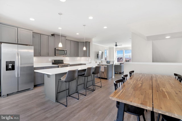 kitchen featuring a breakfast bar area, gray cabinetry, stainless steel appliances, decorative light fixtures, and kitchen peninsula