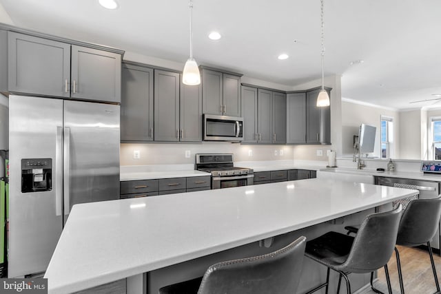 kitchen featuring a breakfast bar, a center island, appliances with stainless steel finishes, gray cabinets, and pendant lighting