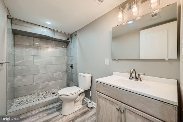 bathroom featuring vanity, hardwood / wood-style flooring, toilet, and tiled shower