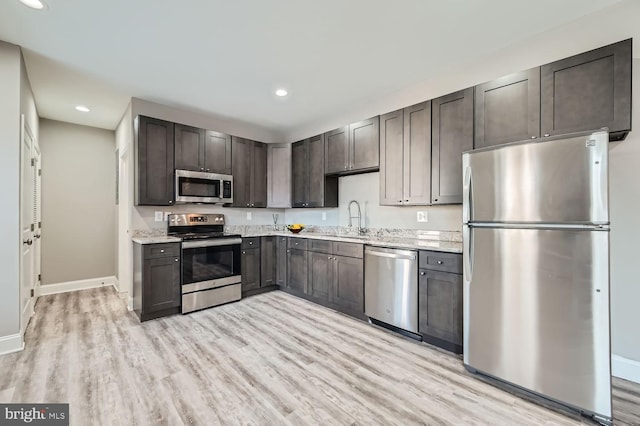 kitchen with dark brown cabinetry, sink, light wood-type flooring, stainless steel appliances, and light stone countertops