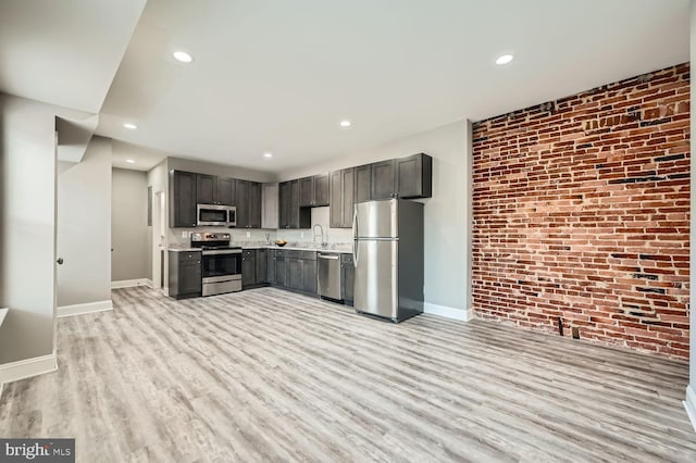 kitchen featuring sink, light hardwood / wood-style flooring, brick wall, and appliances with stainless steel finishes