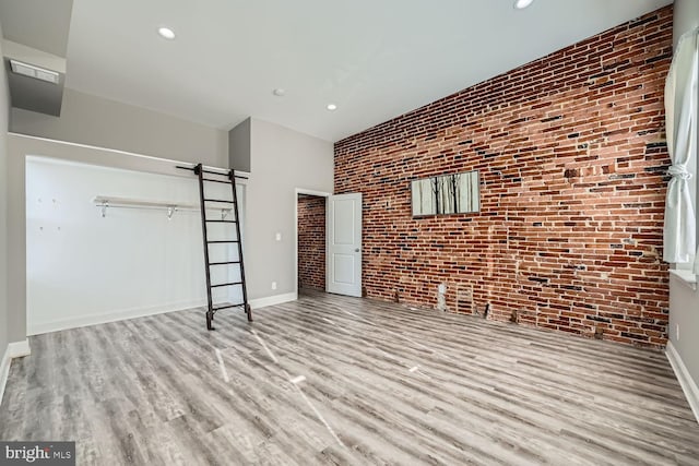 unfurnished living room featuring brick wall and light hardwood / wood-style flooring