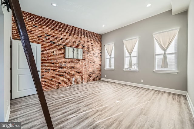 unfurnished living room featuring brick wall and light wood-type flooring