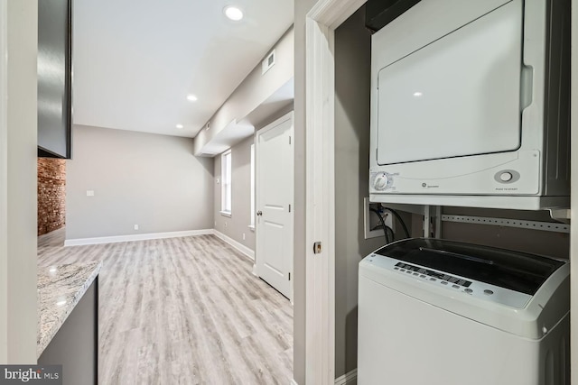 washroom with light hardwood / wood-style flooring, brick wall, and stacked washer / dryer