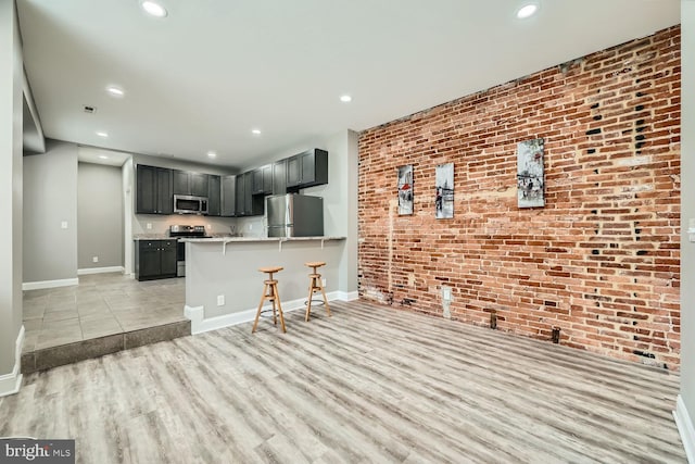 kitchen featuring a breakfast bar, light wood-type flooring, appliances with stainless steel finishes, kitchen peninsula, and brick wall