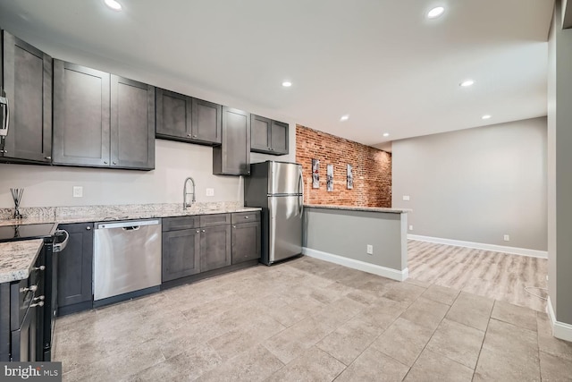 kitchen featuring stainless steel appliances, sink, light stone counters, dark brown cabinets, and brick wall