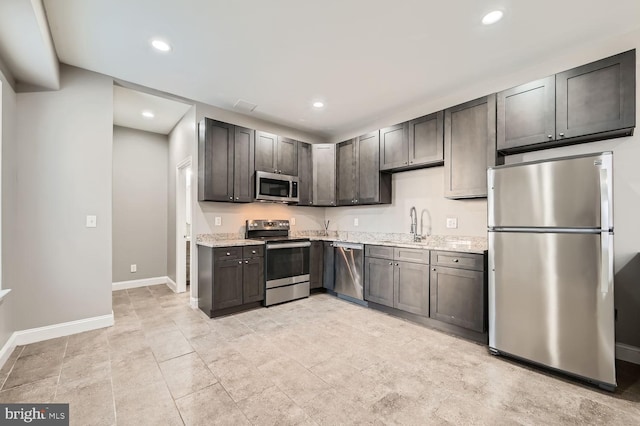 kitchen with stainless steel appliances, light stone countertops, sink, and dark brown cabinets