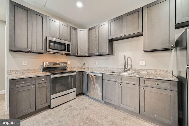 kitchen with stainless steel appliances, light stone countertops, and sink