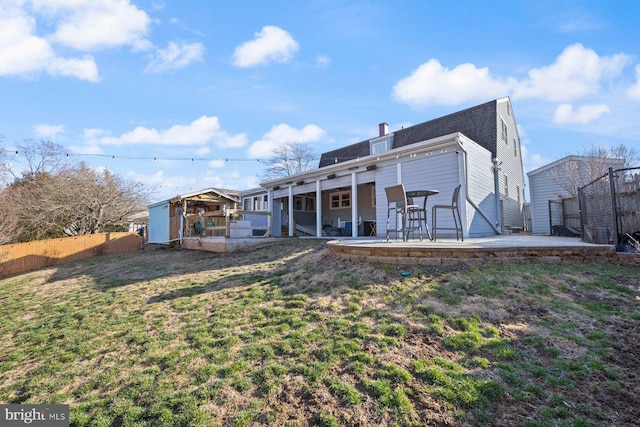 rear view of house with a patio, fence, a yard, a shingled roof, and a chimney