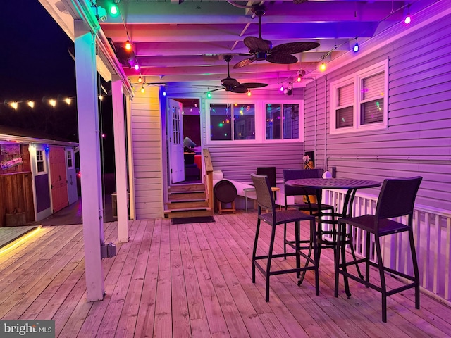 deck at night featuring outdoor dining space and ceiling fan