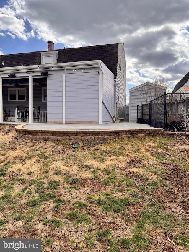 rear view of property with a gate, fence, a chimney, a shingled roof, and a patio area