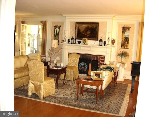 living area with wood-type flooring, a brick fireplace, and ornamental molding