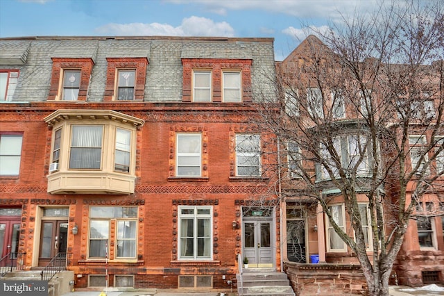 view of property with brick siding, a shingled roof, and mansard roof