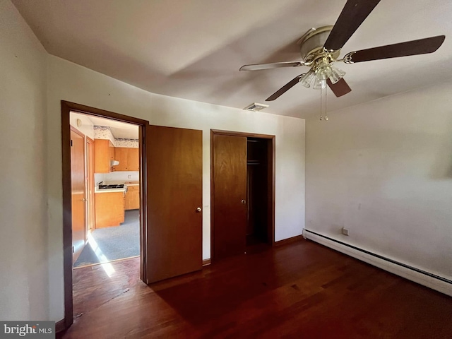 unfurnished bedroom featuring a baseboard heating unit, dark wood-type flooring, and ceiling fan