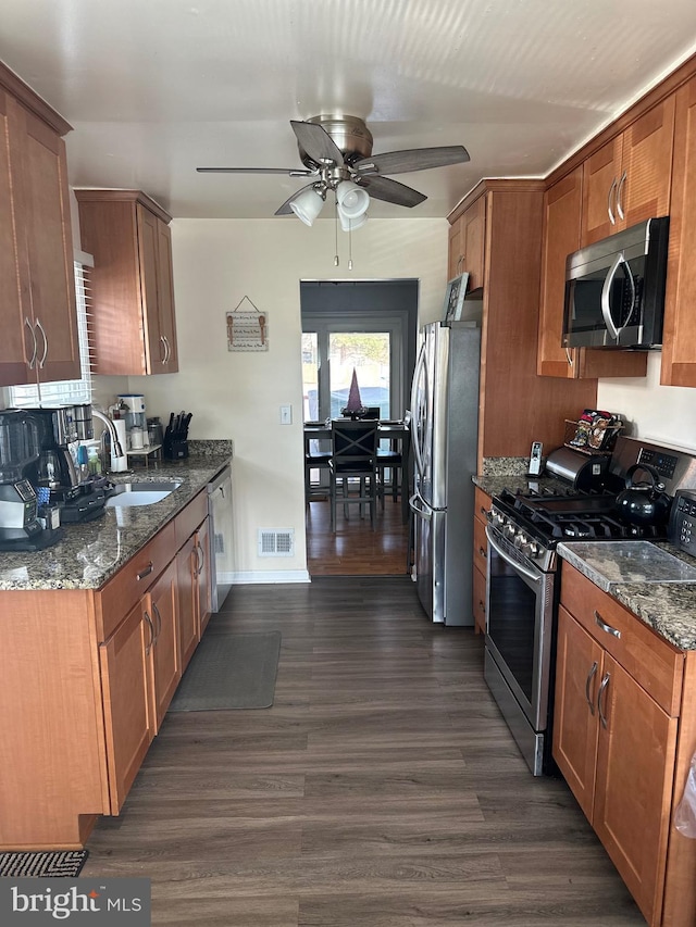 kitchen with dark wood-type flooring, sink, dark stone countertops, appliances with stainless steel finishes, and ceiling fan