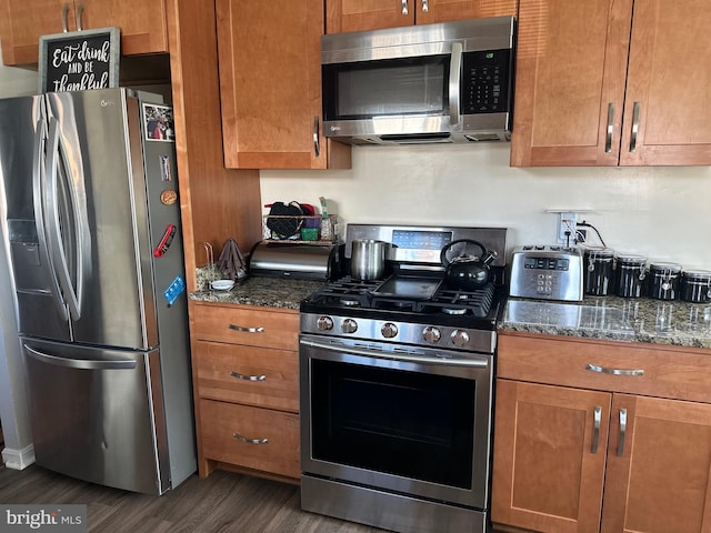 kitchen featuring stainless steel appliances, dark wood-type flooring, and dark stone counters